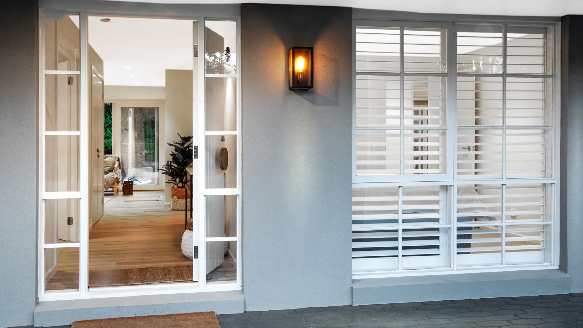 A modern entryway with a glass door leading to a living area, a wall-mounted light, and a window with blinds.