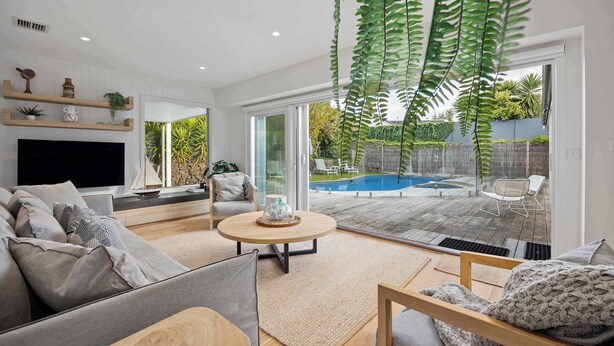 A modern living room with a large TV, comfortable seating, a coffee table, and a view of a backyard with a pool. - Casa del Sol | Indoor Fireplace & Heated Pool (Sorrento)