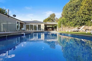 A modern house with a swimming pool, a covered patio, and a lush garden.