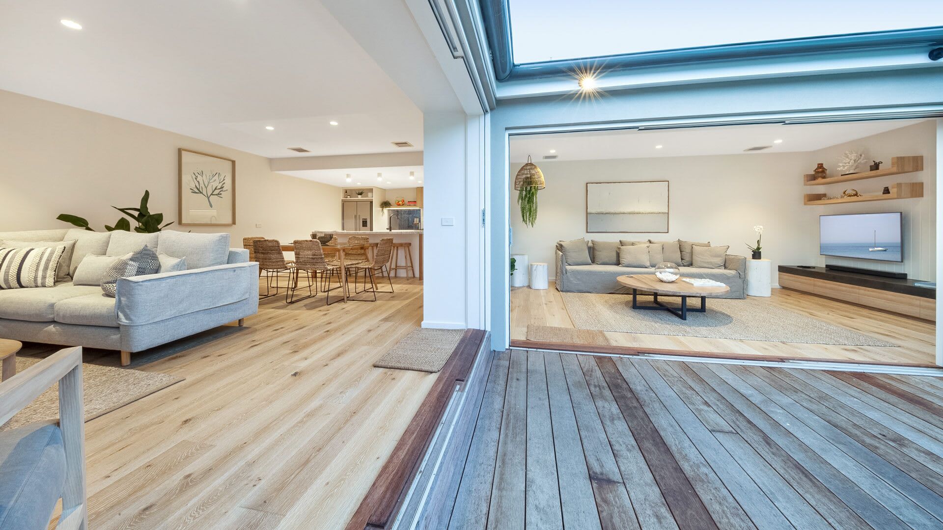 Un salon moderne avec un canapé, une table basse et un téléviseur. Il y a également un coin repas avec des chaises et une table. La pièce est dotée d’un parquet et d’une grande fenêtre.