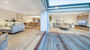 A modern living room with a sofa, coffee table, and TV. There is a dining area with chairs and a table. The room has wooden flooring and a large window. - Casa del Sol | Indoor Fireplace & Heated Pool (Sorrento)