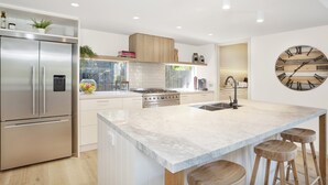 A modern kitchen with a stainless steel refrigerator, a built-in oven, a large marble island with stools, and a wooden ceiling. - Casa del Sol | Indoor Fireplace & Heated Pool (Sorrento)