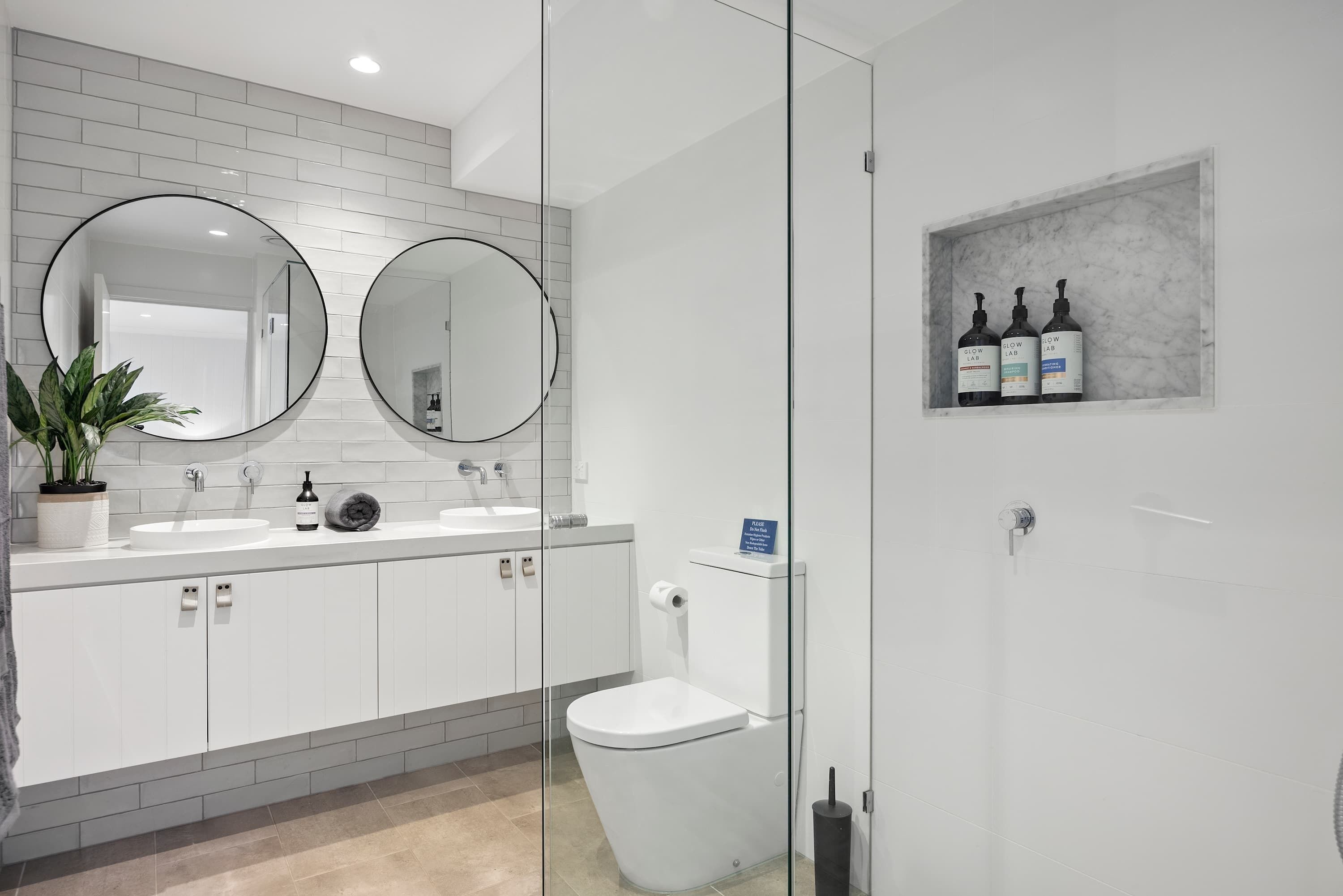 Ein modernes Badezimmer mit einem weißen Waschbecken, zwei runden Spiegeln, einer Toilette und einer Duschkabine.