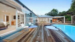 A modern outdoor pool area with wooden decking, lounge chairs, and a covered seating area. - Casa del Sol | Indoor Fireplace & Heated Pool (Sorrento)