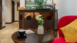 A reception area with a decorative ceiling, a reception desk, a vase with flowers, a coffee cup, and a red couch with a pillow. - Westlake Lion Boutique Studio & Spa (Hanoi)