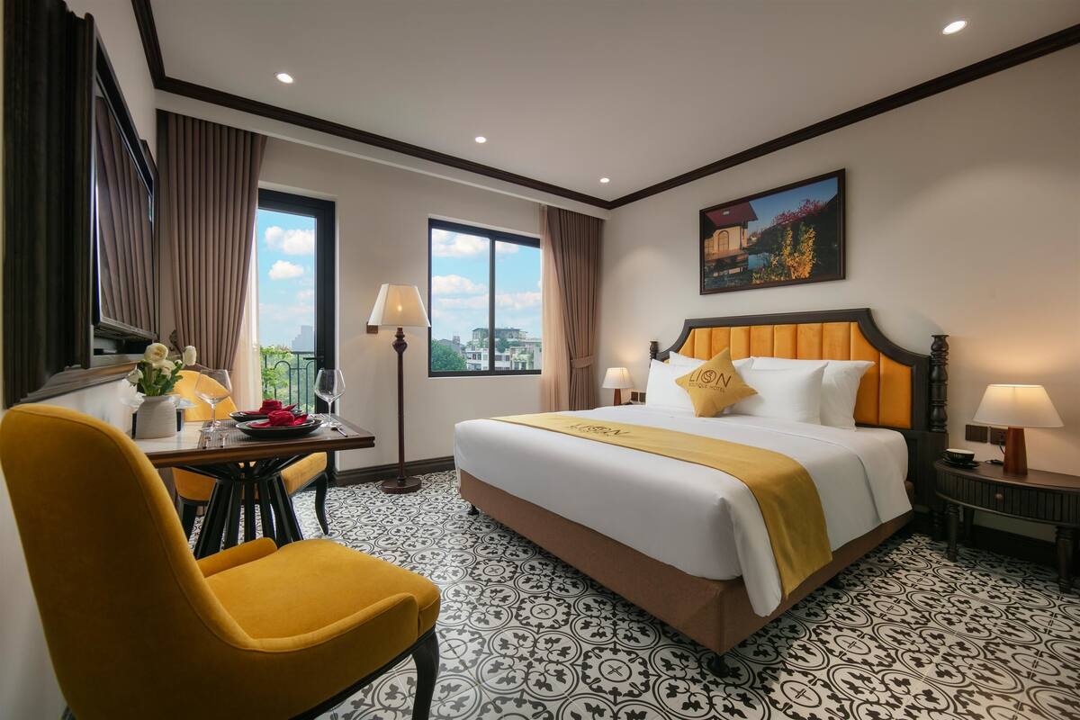 A hotel room with a large bed, a desk with a chair, a window with curtains, and a painting on the wall.