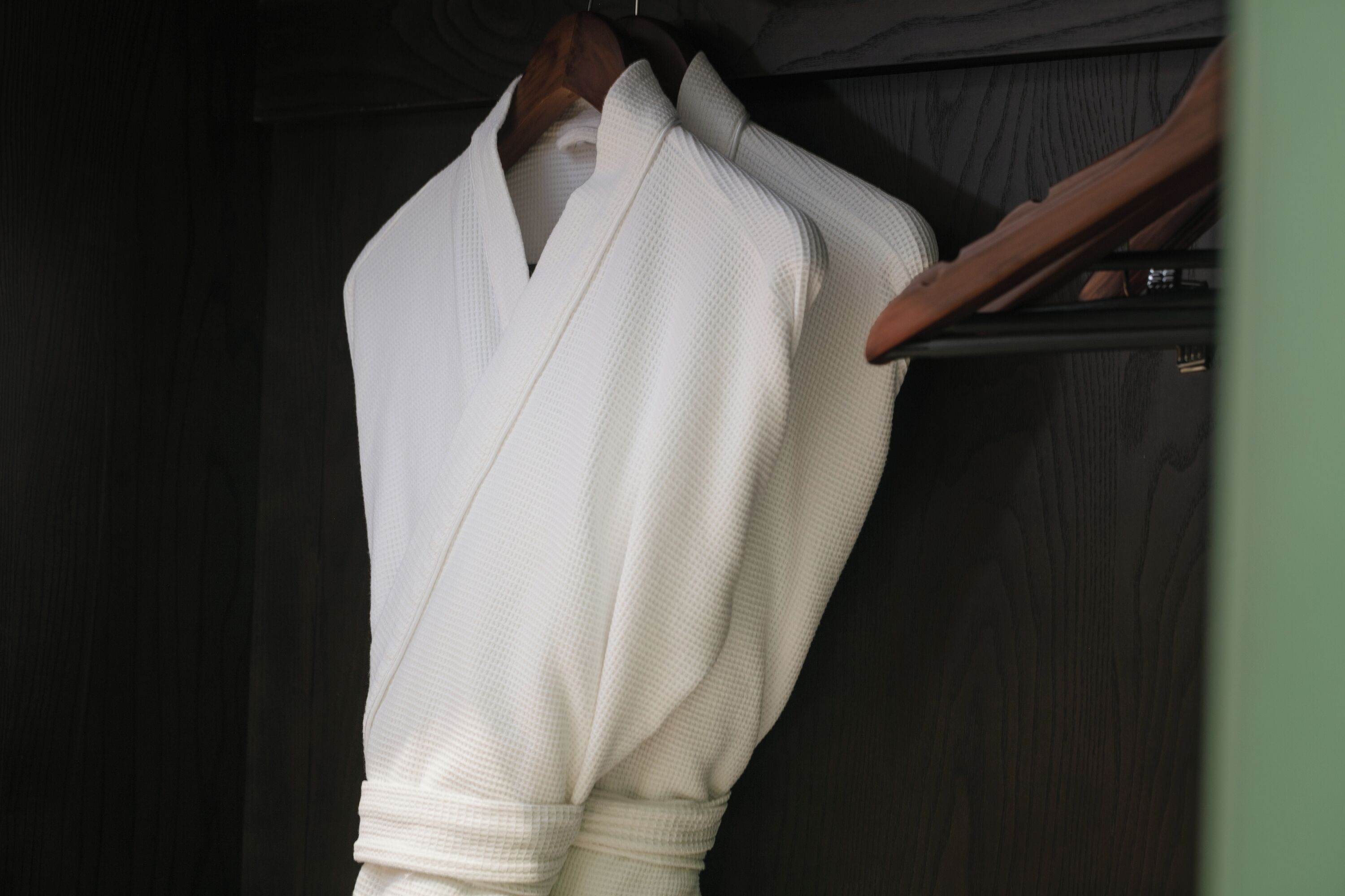 A white robe hanging on a wooden hanger against a dark wooden background.