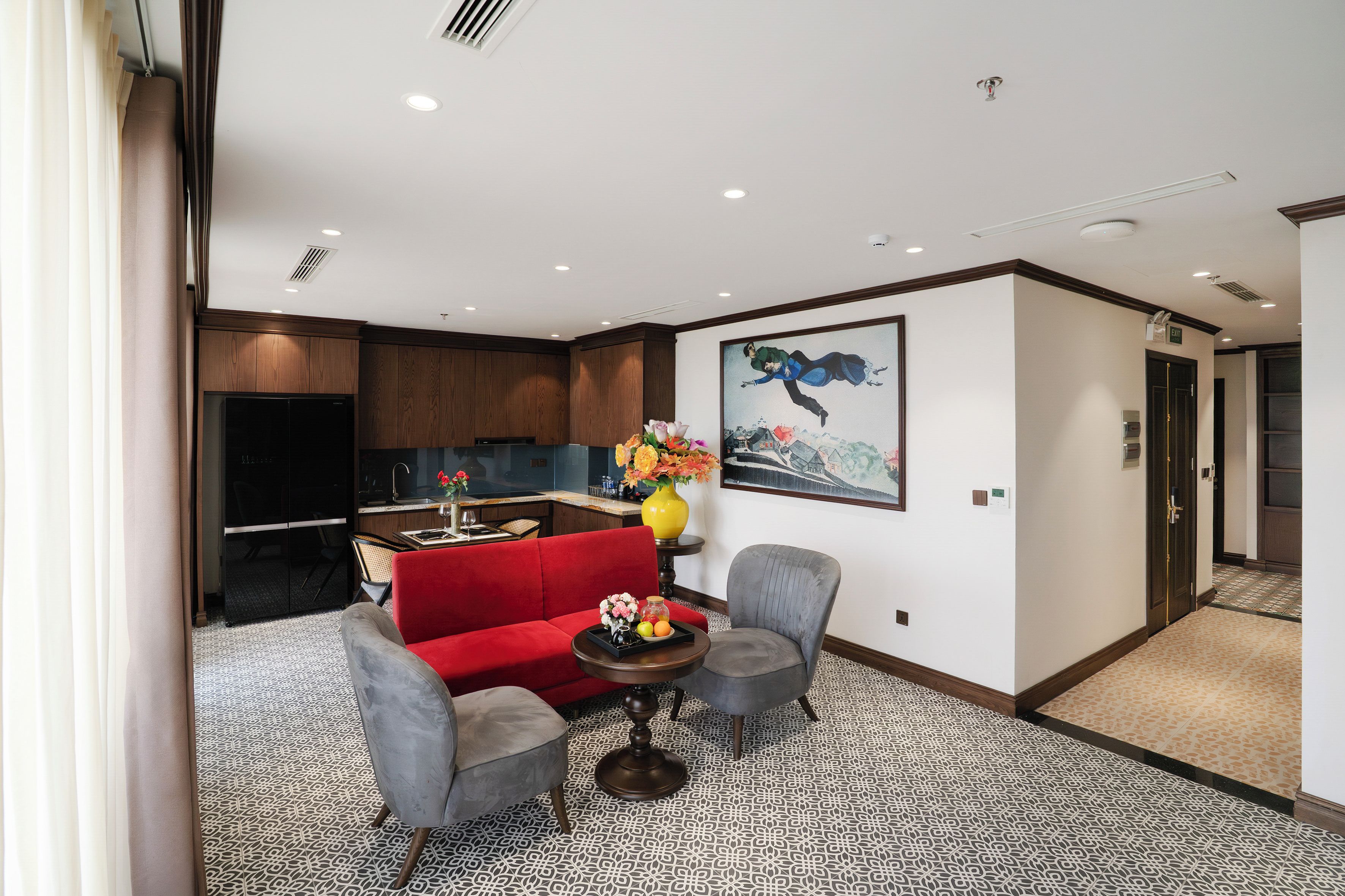 A modern living room with a red sofa, grey armchairs, a coffee table, and a kitchen in the background.