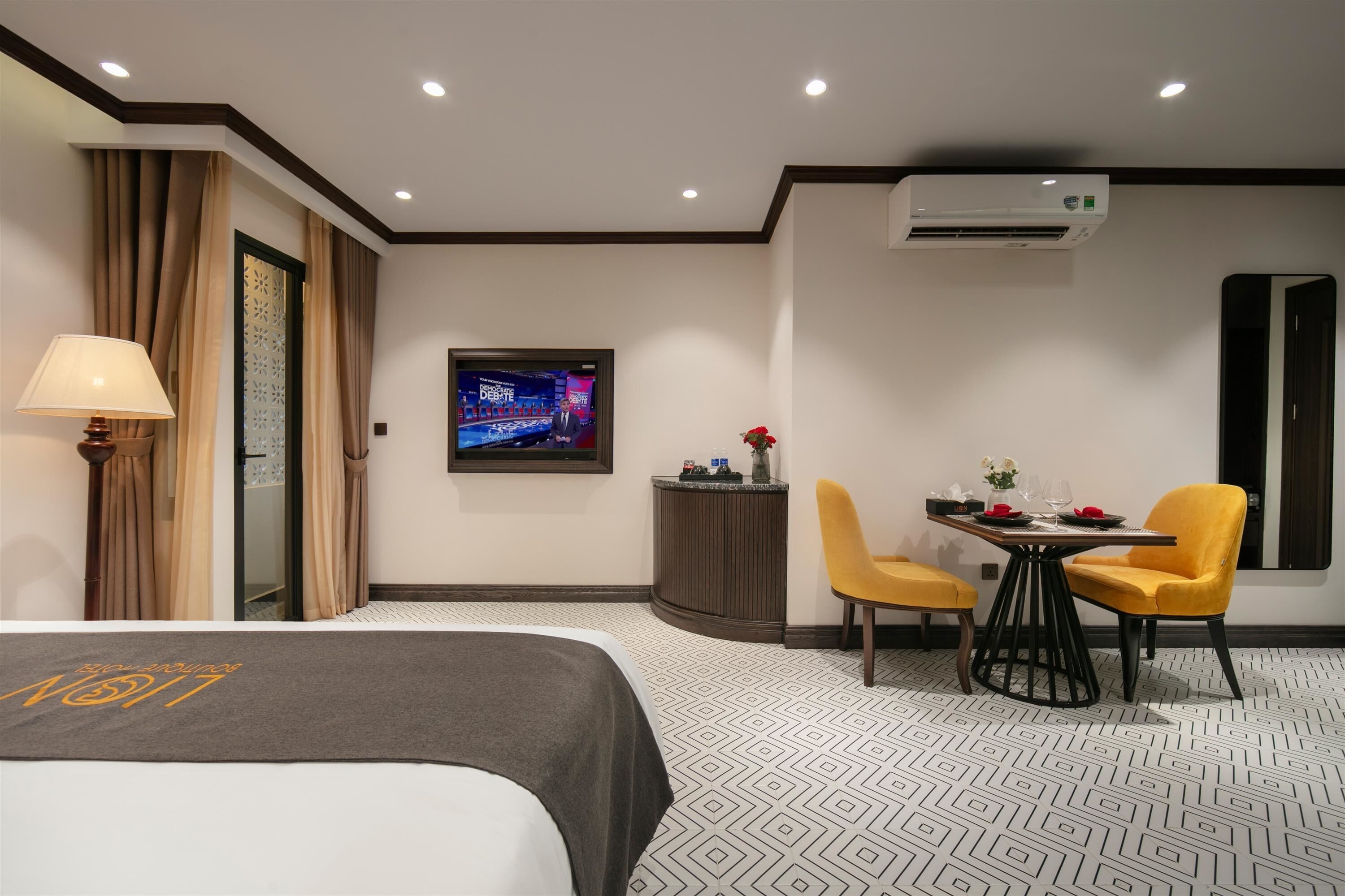 A hotel room with a bed, a TV, a dining table with chairs, and an air conditioning unit.