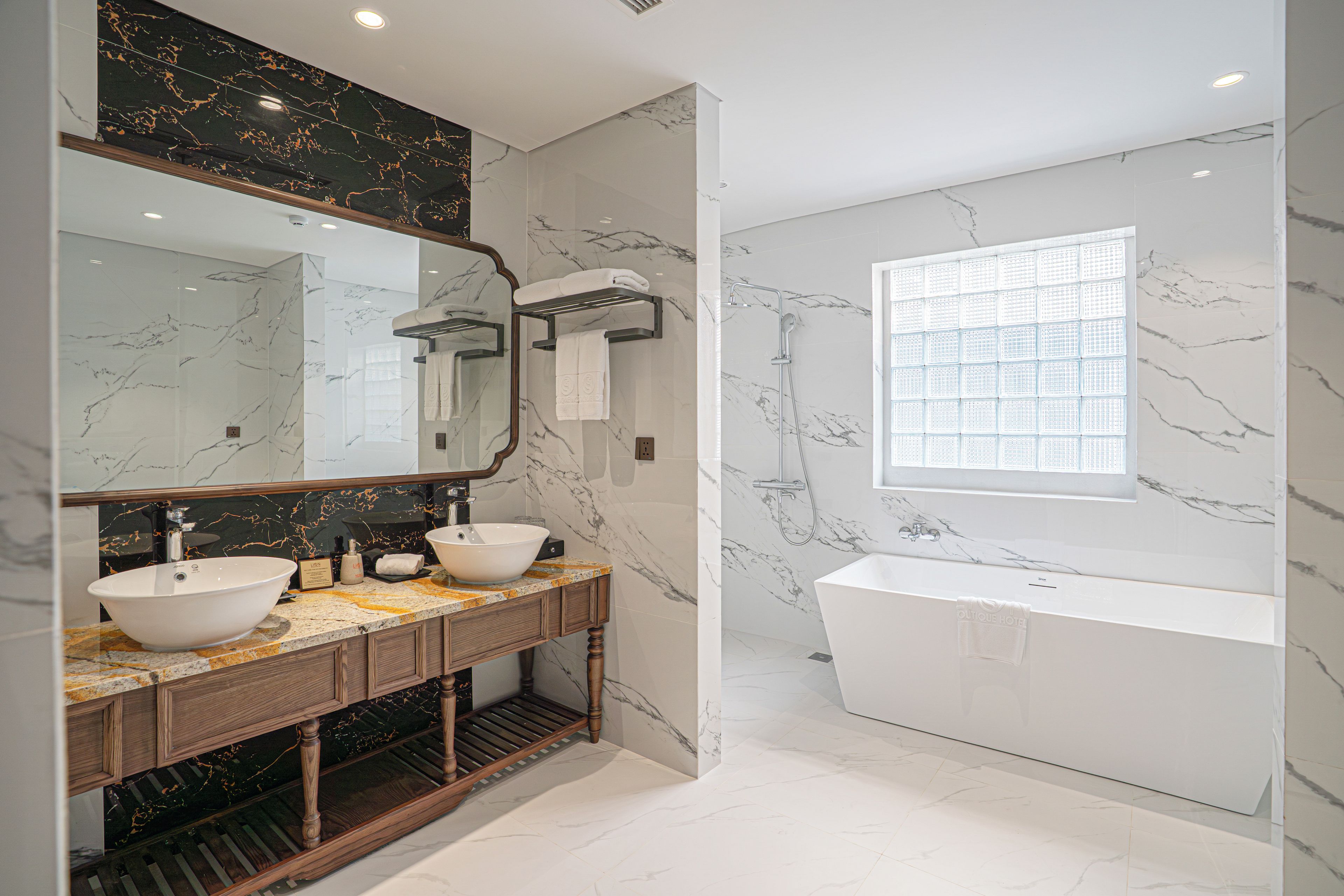 Une salle de bain moderne avec un grand miroir, deux lavabos, une baignoire et une fenêtre.