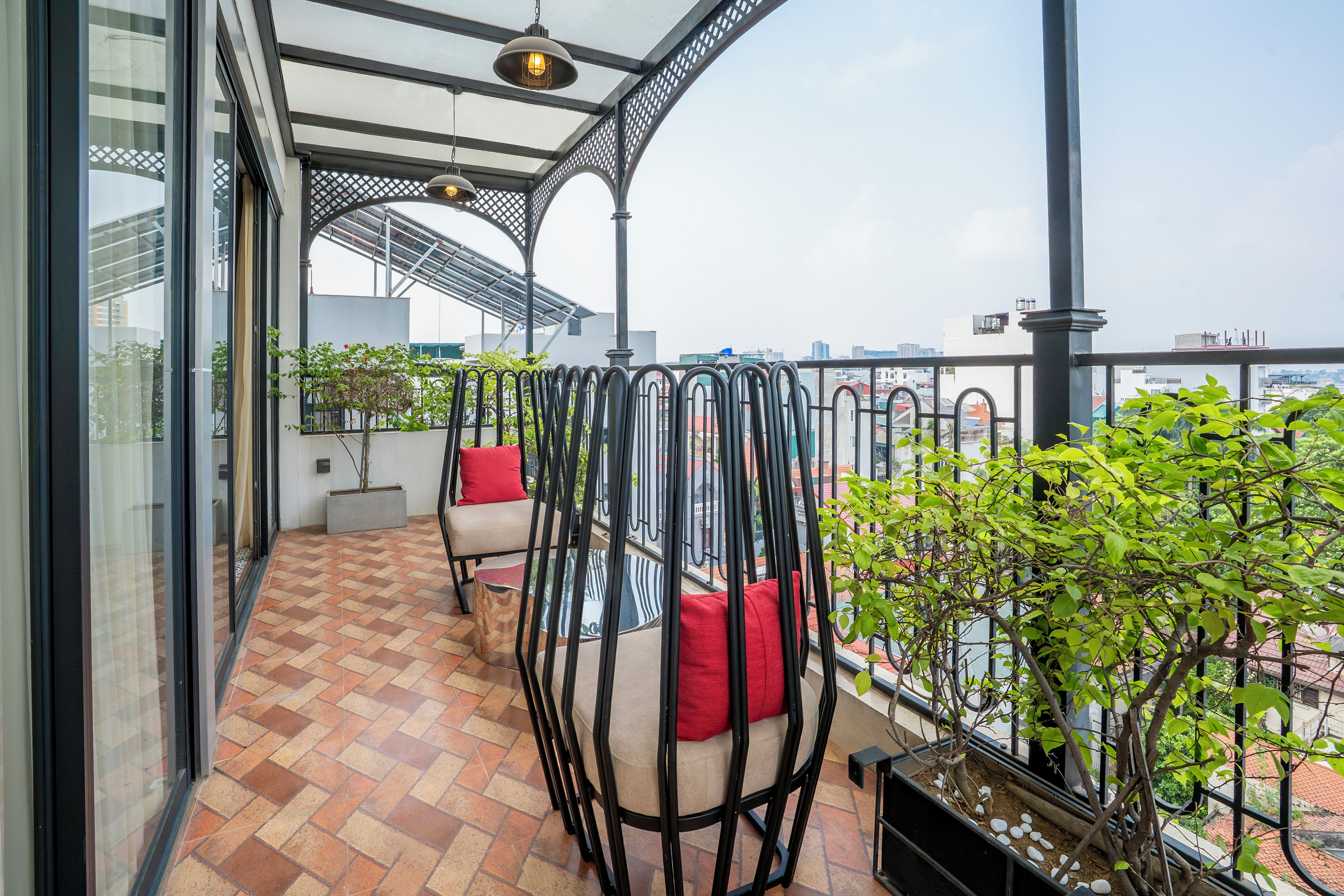 A balcony with a tiled floor, a seating area with cushions, a potted plant, and a view of the cityscape.