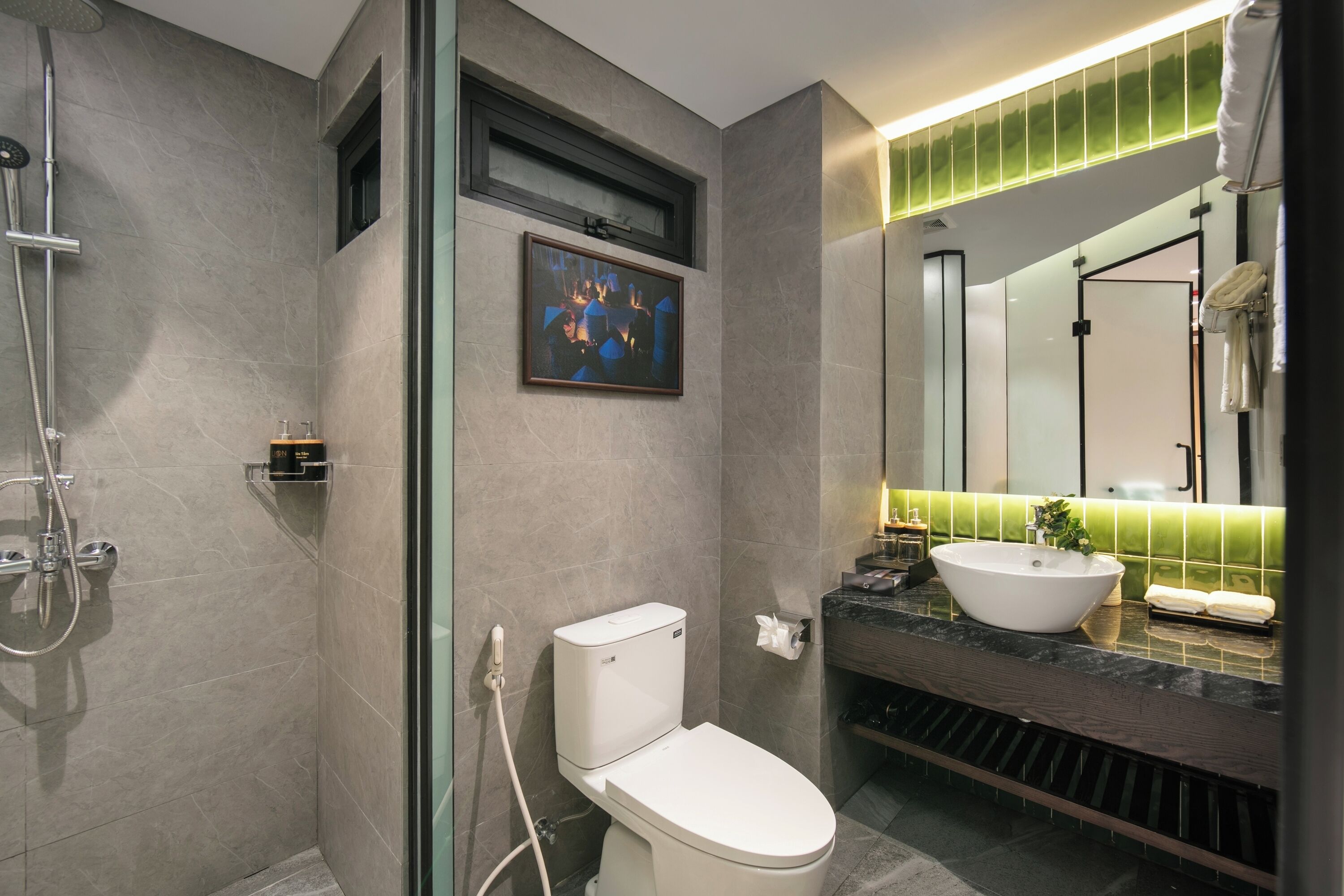 A modern bathroom with a glass-enclosed shower, a toilet, a sink with a vessel basin, and a large mirror with a green-tiled backsplash.
