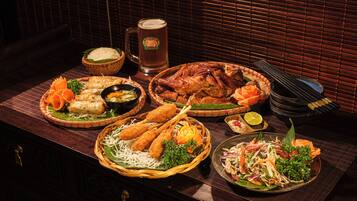 A variety of dishes including rice, fried items, and a salad, arranged on a table with a beer mug and bowls.