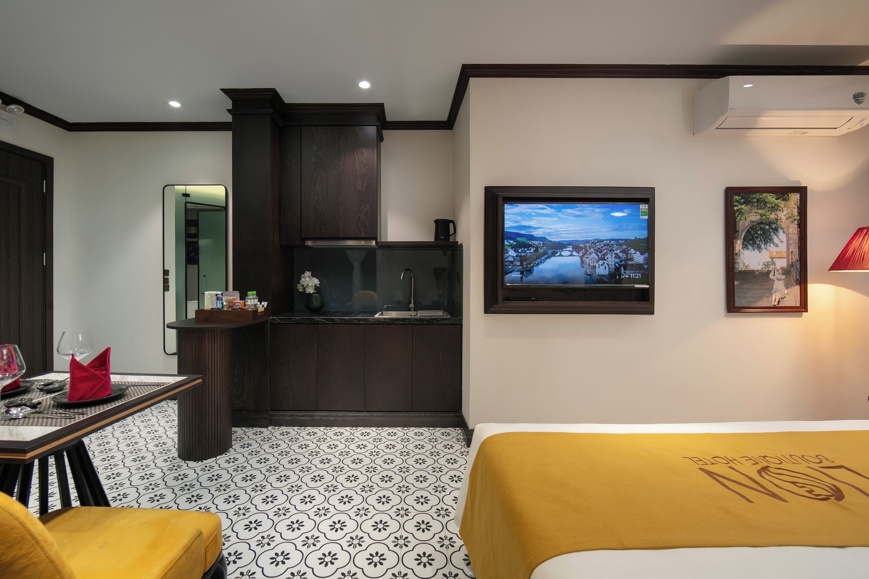 Une chambre d’hôtel avec un lit, une petite kitchenette, une télévision et un tableau encadré au mur.