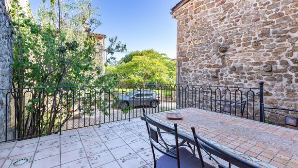 Une terrasse avec une table et des chaises, un mur en pierre et un arbre.