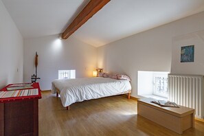 Ein Schlafzimmer mit Bett, Holzboden, Fenster und Heizkörper sowie einem kleinen Tisch.