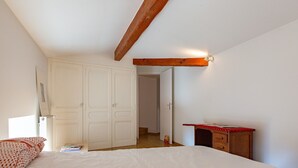 Une chambre à coucher comprenant un lit, un bureau en bois, une armoire et une porte donnant sur une autre pièce.