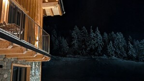 A wooden building with a balcony, stone foundation, and a snowy landscape in the background.