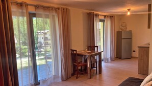 A cozy room with a wooden dining table, chairs, a sofa, and a refrigerator.