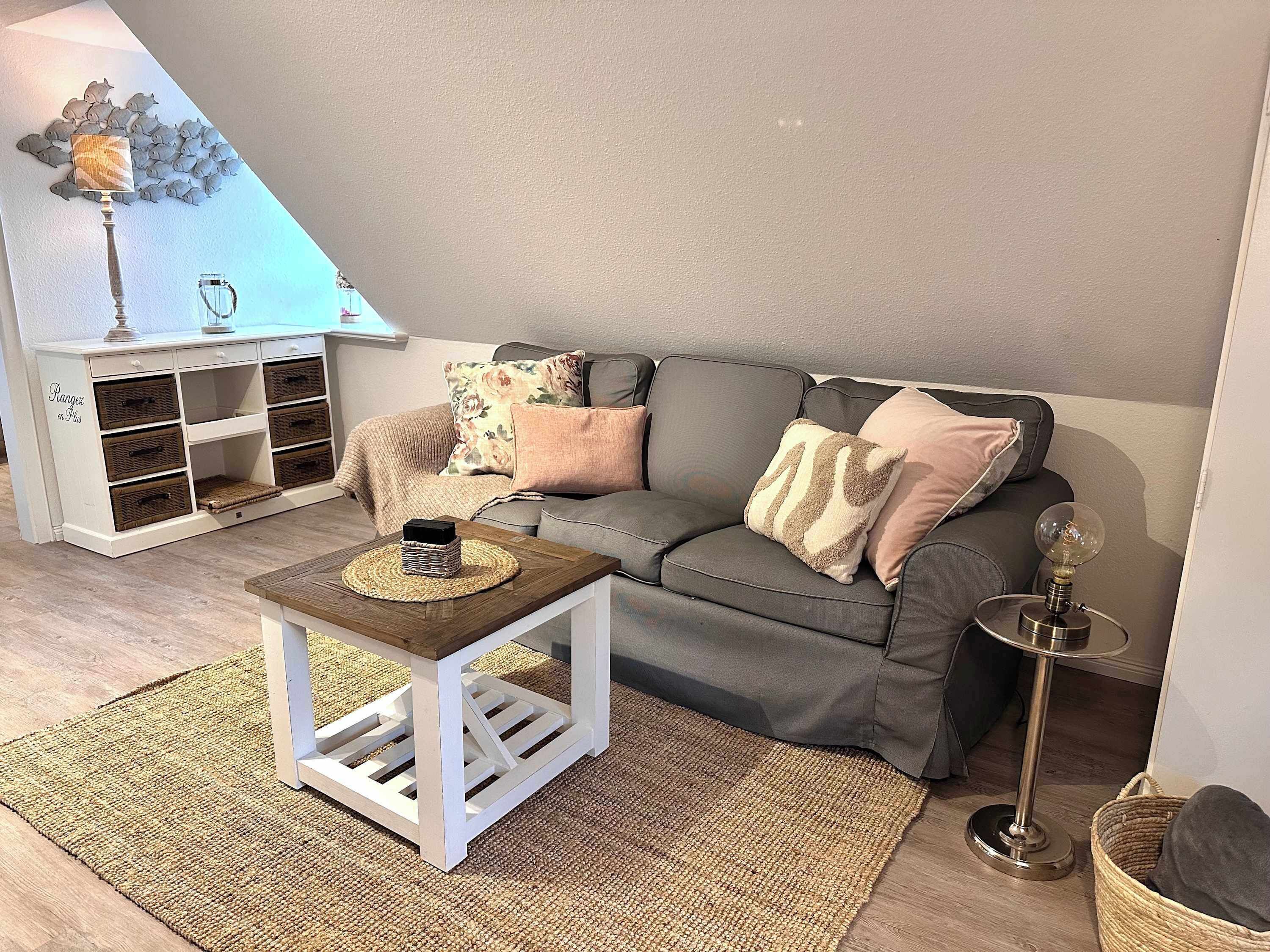 Una sala de estar acogedora con un sofá gris, una mesita blanca y un adorno de pared decorativo.