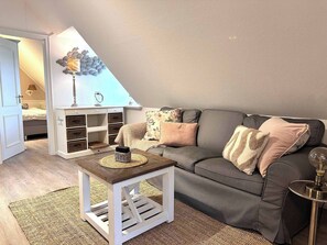 A cozy loft bedroom with a grey sofa, a small white table, and a decorative wall piece.