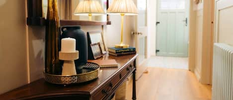 A hallway with a wooden dresser, a vase, a candle, a lamp, and a radiator.