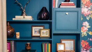 Una estantería con libros, un florero y cuadros enmarcados.