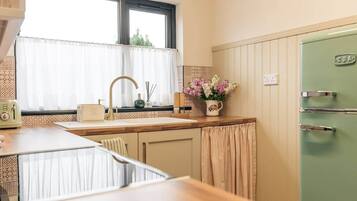 Una cocina con ventana, un lavamanos, un tostador antiguo y un refrigerador verde.