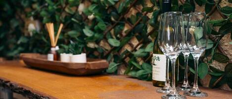 A wooden bar counter with three wine glasses and a bottle of wine, surrounded by greenery.