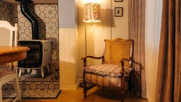 Une pièce avec un poêle ancien, une chaise en osier, un lampadaire et un papier peint à motifs.