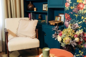 Une pièce comprenant une chaise, une bibliothèque et un arrangement floral.