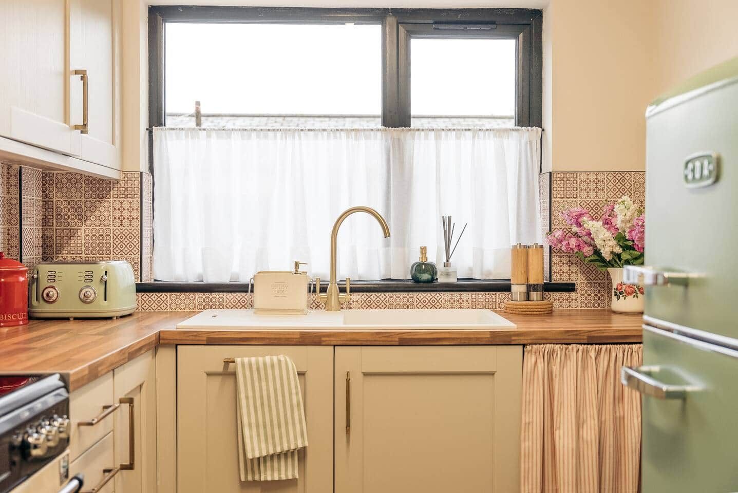 A kitchen with a window, a sink, a vintage toaster, and a refrigerator.