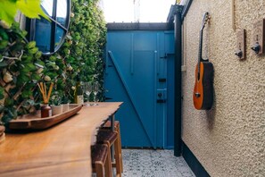 Una mesa de madera con vasos y una botella, una puerta azul y una guitarra en la pared.