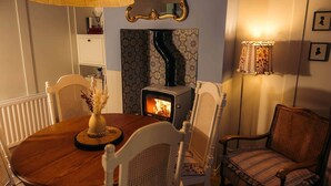 A cozy room with a round wooden table, white chairs, a wood-burning stove, and a patterned wallpaper. - No. 50 Chapel Street (Cookstown)