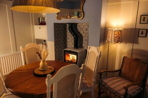 A cozy room with a round wooden table, white chairs, a wood-burning stove, and a patterned wallpaper.