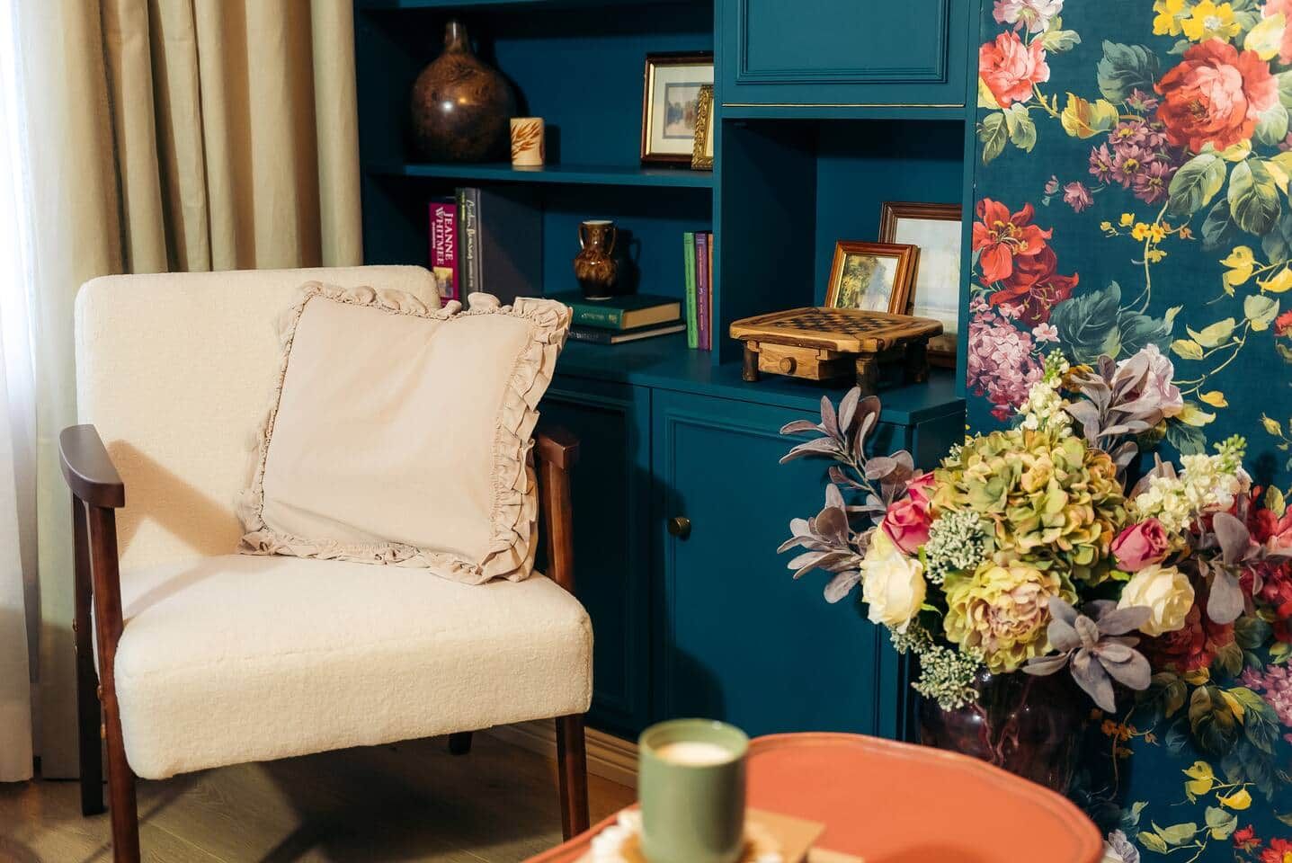 A room with a chair, a bookshelf, and a floral arrangement.