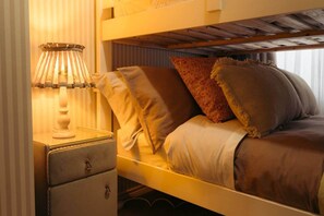 Una cama litera con cabecera, una mesita de noche con lámpara y un mueble con cajones.