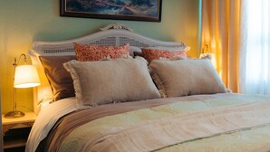 A bed with a white headboard, multiple pillows, a patterned bedspread, and a painting above the bed.