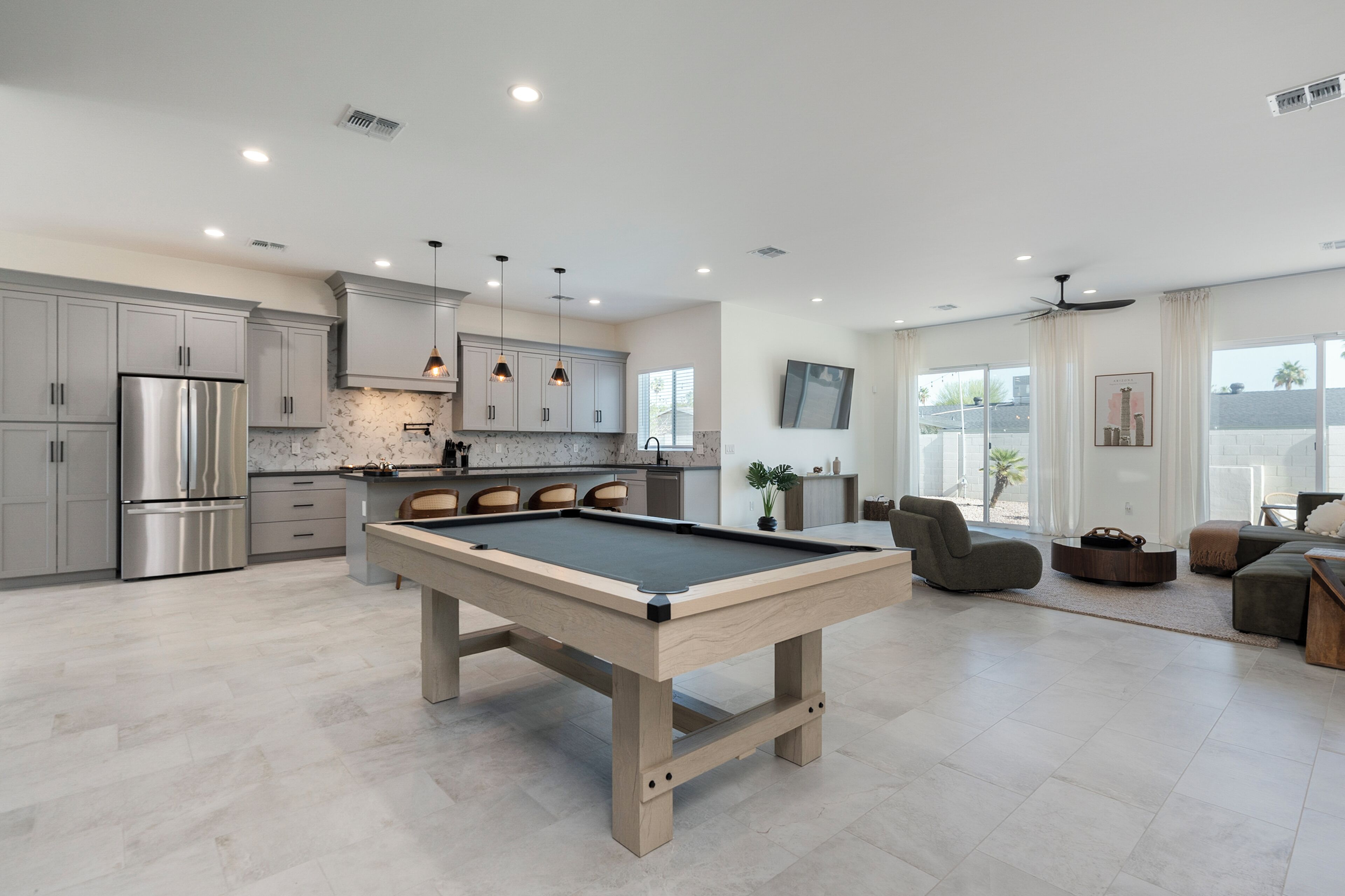 Una cocina moderna con mesa de billar, armarios grises y refrigerador de acero inoxidable.