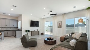 Ein modernes Wohnzimmer mit Sofa, Sessel und Couchtisch, eine Küche mit weißen Schränken und ein großes Fenster mit Ausblick.