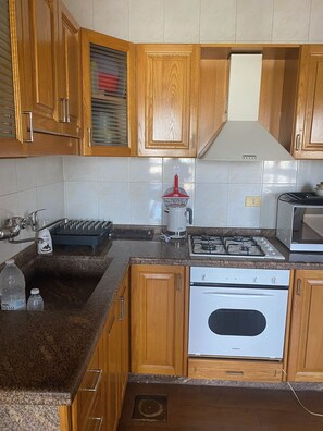 A kitchen with wooden cabinets, a granite countertop, a stainless steel range hood, a gas stove, an oven, and a microwave.