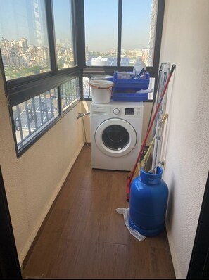 A laundry room with a washing machine, a blue gas cylinder, and cleaning supplies.