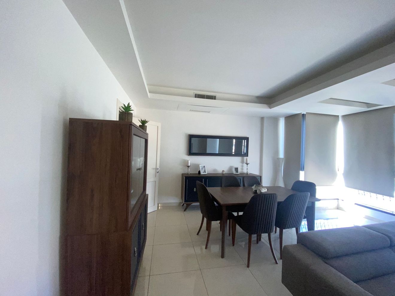 A modern living room with a dining area, a built-in TV, and a large window providing natural light.