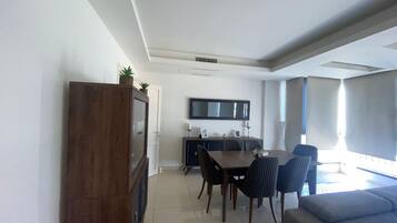 A modern living room with a dining area, a built-in TV, and a large window providing natural light.