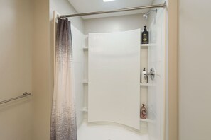 Un bagno con tenda doccia, portasciuga e ripiano con articoli da toilette.