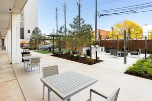 Un'area patio all'aperto con tavoli e sedie, circondata da vegetazione e un muro in mattoni.