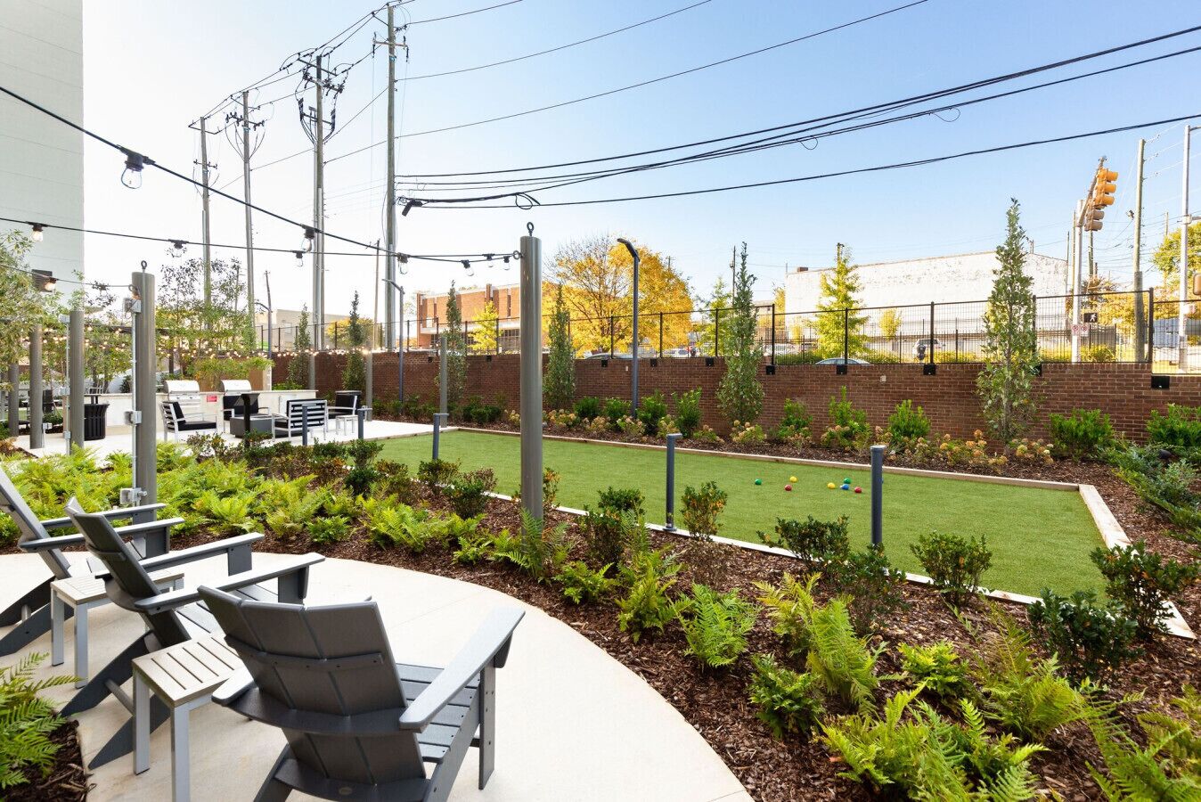 An outdoor seating area with tables and chairs, a small lawn, and a brick wall in the background.