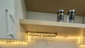 A kitchen with a countertop, a sink, a kettle, and a shelf with jars and a string of lights.