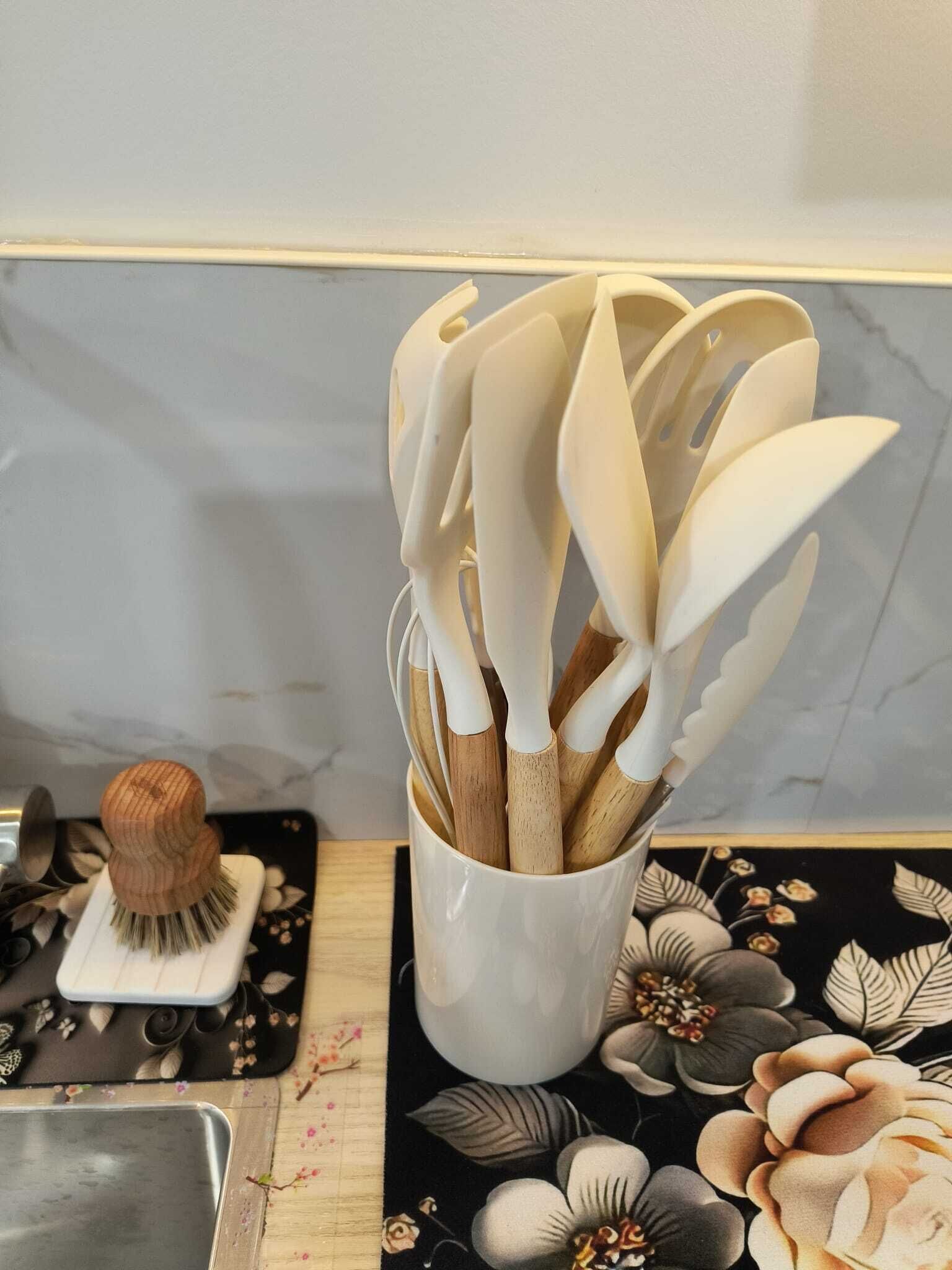 Eine Küchenarbeitsplatte mit einer weißen Keramiktasse, die Holdbesteck, einen Holzpinsel und eine schwarze Ablage mit floralen Mustern enthält.