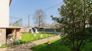 Un jardin avec un mur en pierre, un barbecue, une zone délimitée par une clôture et une pelouse.